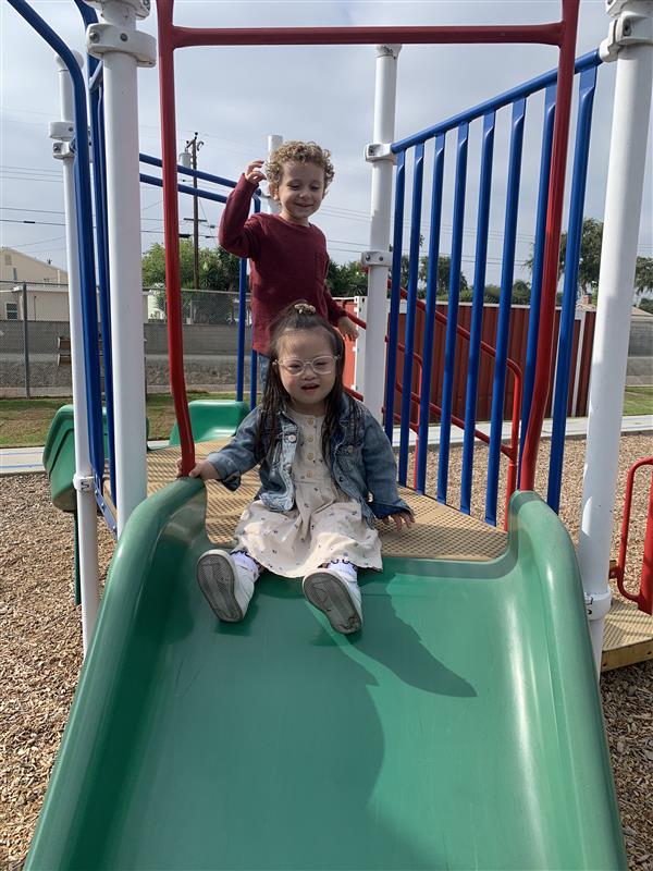 Two students going down the playground apparatus